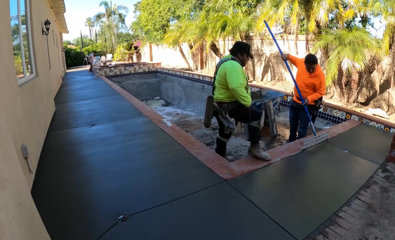 Concrete pool deck being installed by a crew around a residential swimming pool